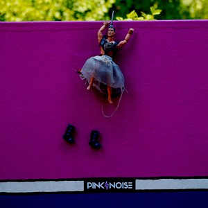 Poupée masculine habillée d'une jupe suspendu sur un panneau rose et bleu au dessus de ses bottes et inscription Pink Noise - France  - collection de photos clin d'oeil, catégorie clindoeil